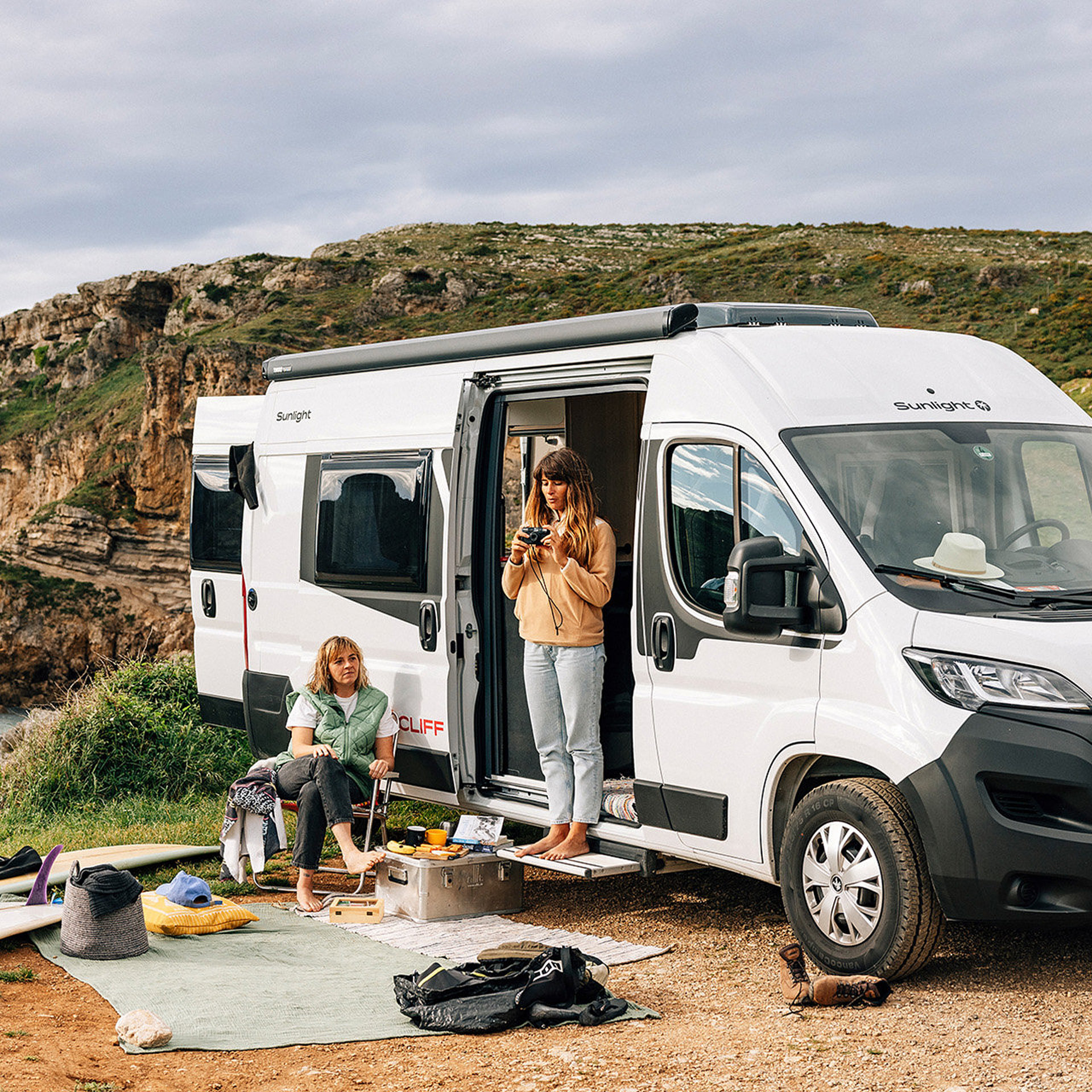 Zwei Frauen genießen den Morgen vor ihrem Reisemobil direkt an der Küste. 