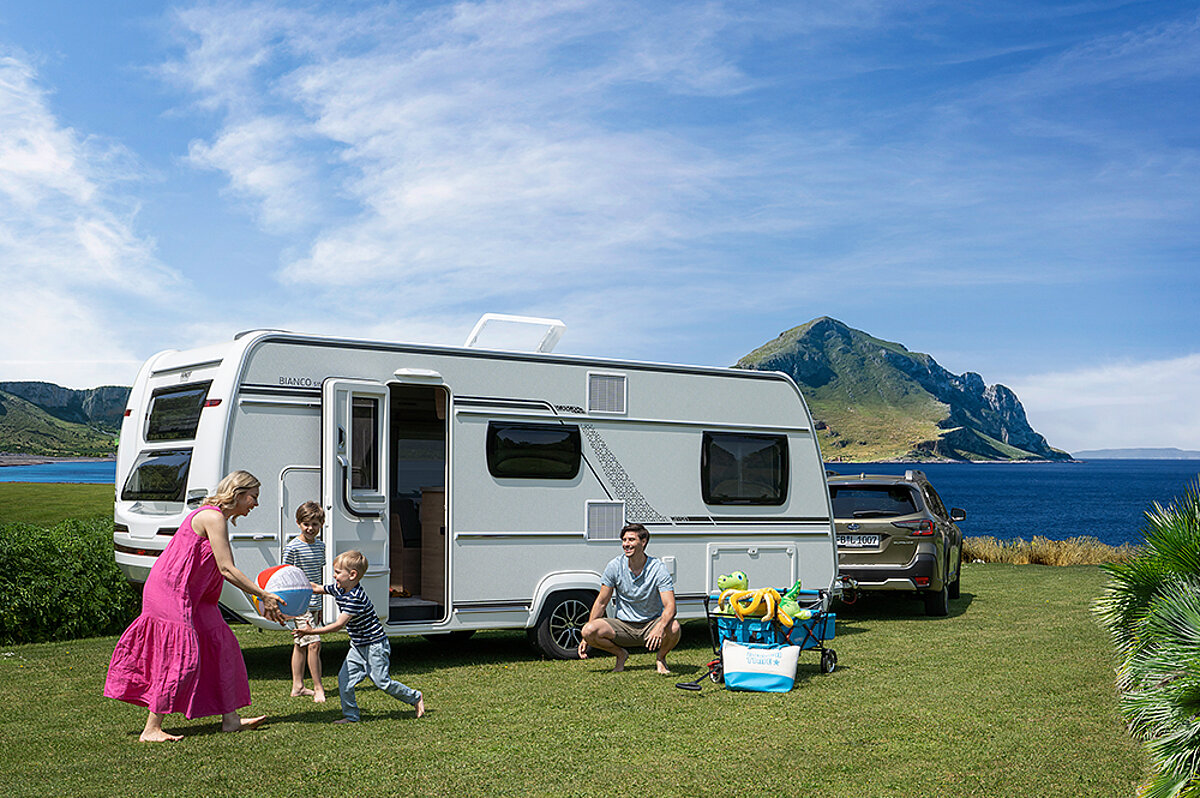 Eine Familie mit zwei Kindern spielt vor einem Wohnwagen.
