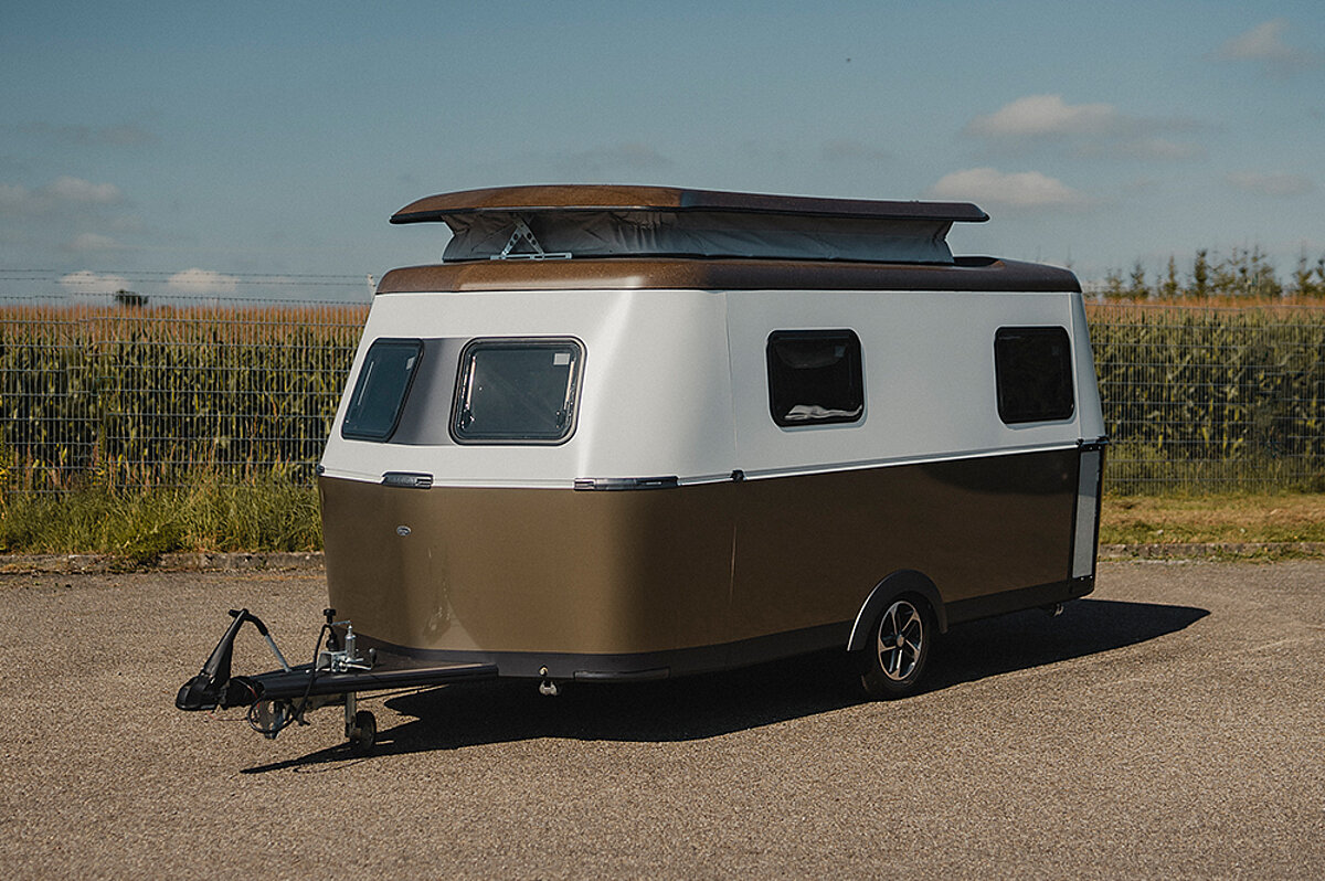 Ein kompakter Wohnwagen steht vor einem Feld.
