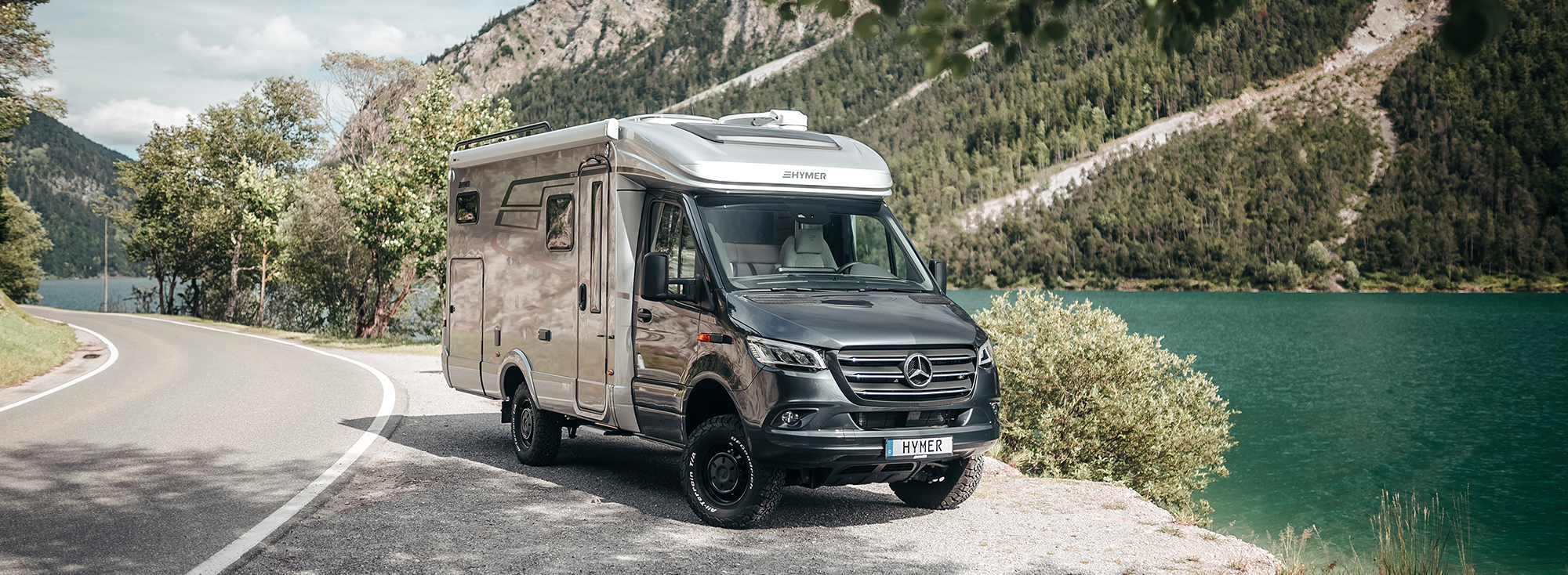 Ein gebrauchtes Wohnmobil steht auf einem Standstreifen neben einem See. 