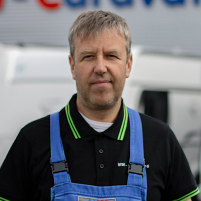 Marcus Siebeneicher ist als Werkstattleiter immer für Sie da! Werkstattleiter Marcus Siebeneicher steht in Arbeitskleidung vor dem Gebäude von MW-Caravaning.