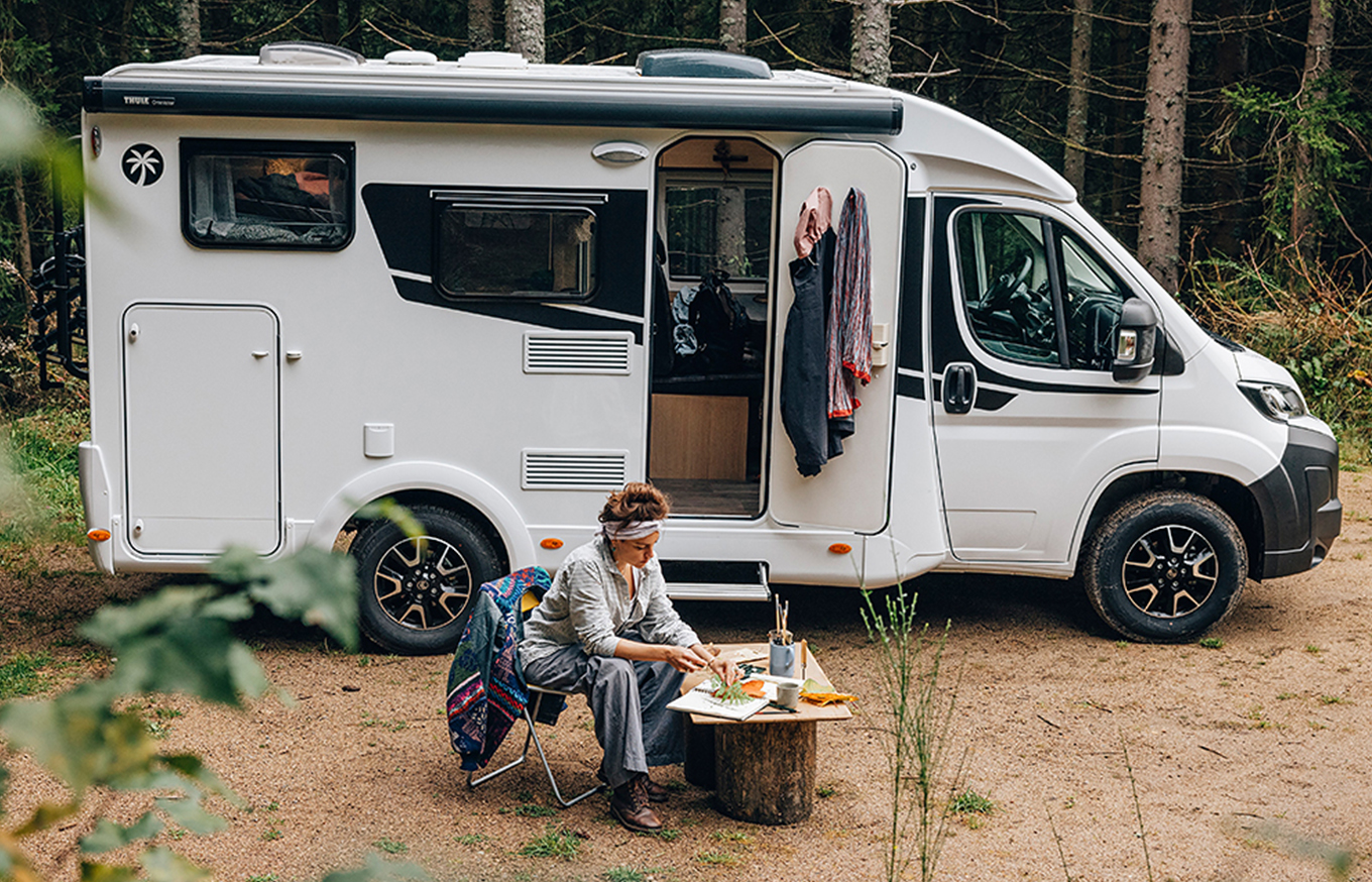 Kaufen Sie Ihr Sunlight Wohnmobil bei MW-Caravaning! Eine Frau isst vor ihrem Wohnmobil von Sunlight auf einer Waldlichtung.